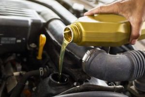 Car mechanic replacing and pouring fresh oil into engine at maintenance repair service station.